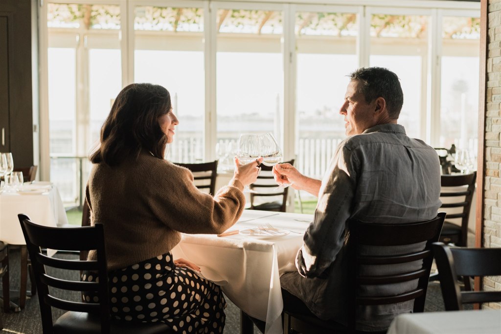 Man and woman toast while dining at Seafire On The Marina, Glenelg. 