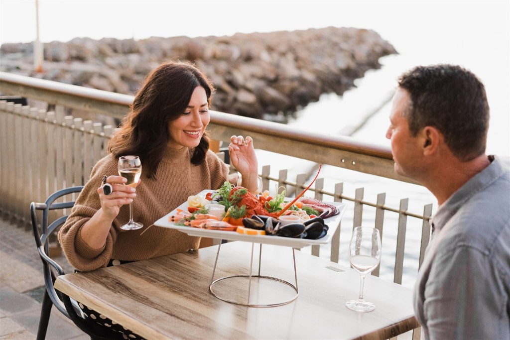 Woman smiling, holding glass of wine and peering into seafood platter.